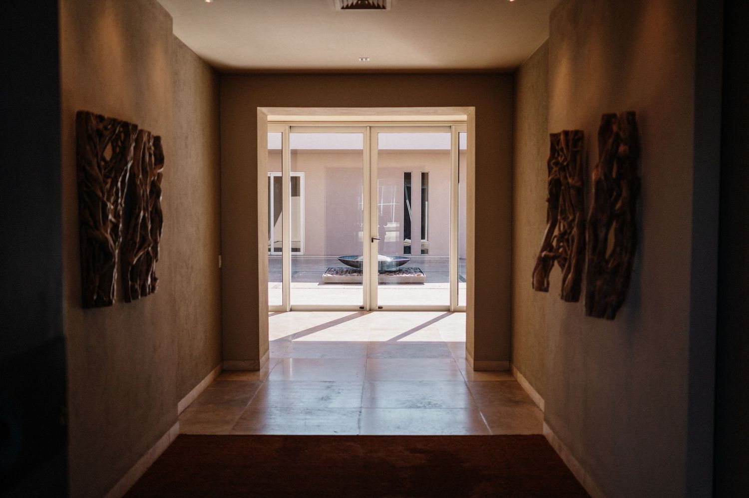 Elegant hallway with decorative wall art leading to bright French doors opening to a sunlit courtyard.