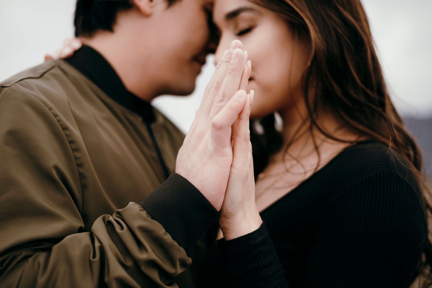 Intimate moment captured between couple with clasped hands against white background.