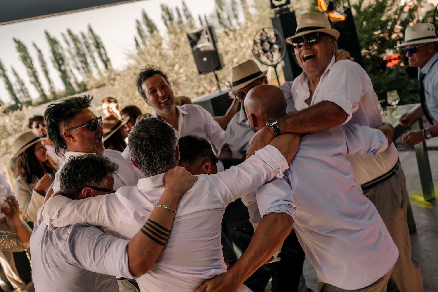 A group of people in white shirts celebrate and embrace during an outdoor gathering at sunset.