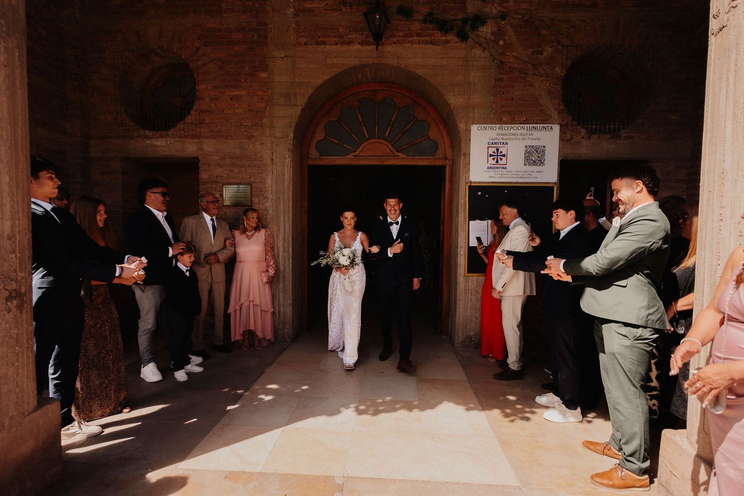 A wedding party dances in a dimly lit brick-walled venue during a reception celebration.
