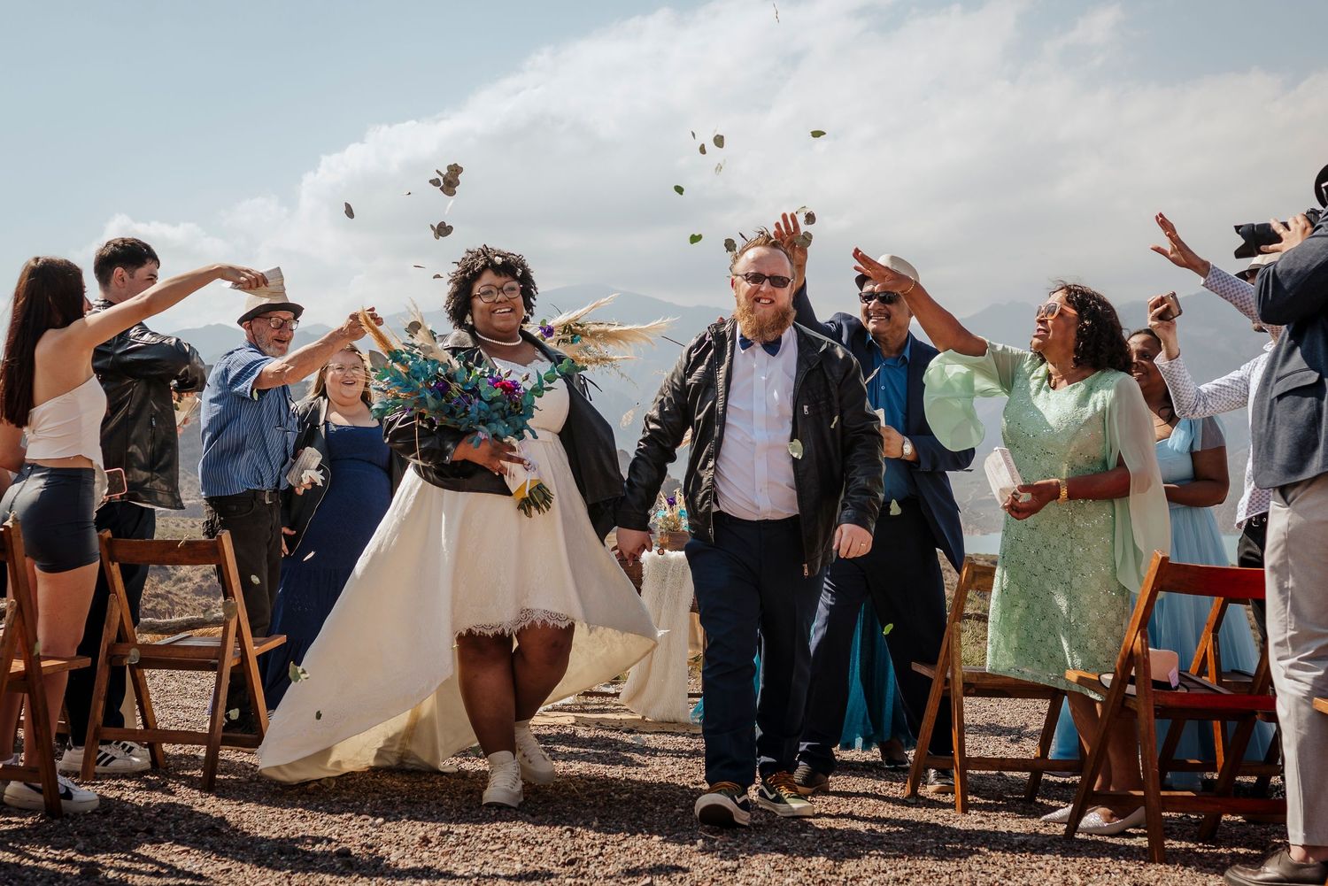 Wedding celebration with guests tossing confetti in the air against blue sky.