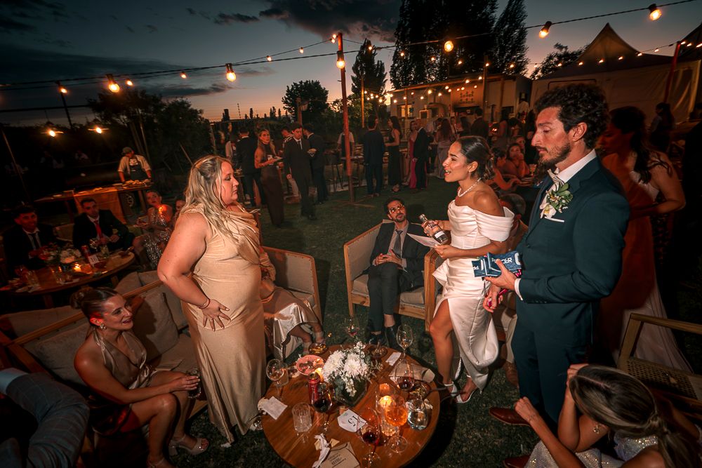 Wedding guests dance and celebrate under string lights at an outdoor evening reception.