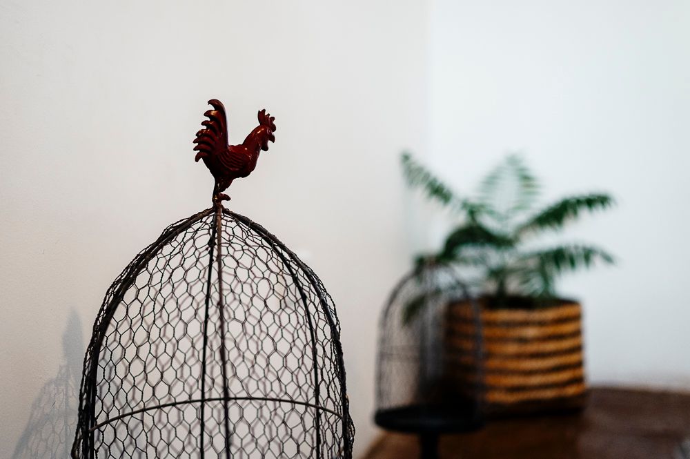 Decorative metal wire rooster sculptures and ornamental birdcages displayed on wooden surfaces in a rustic home setting.