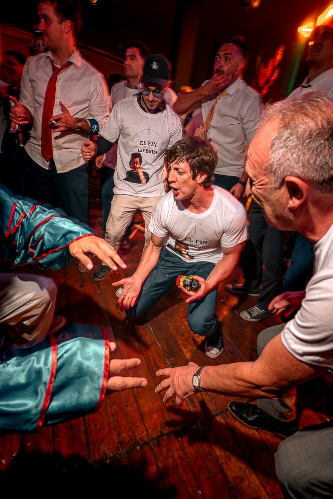 Energetic crowd dances and jumps at a dimly lit nightclub with orange lighting and wooden floors. wedding in mendoza