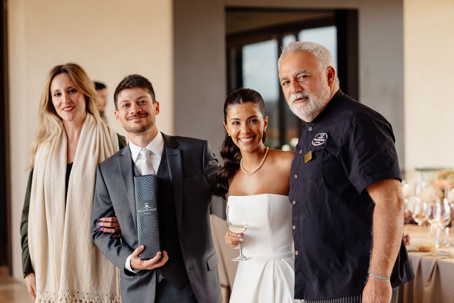 Wedding couple poses with two guests at elegant indoor reception venue, bride in white dress, groom in gray suit. fotógrafos de boda Mendoza