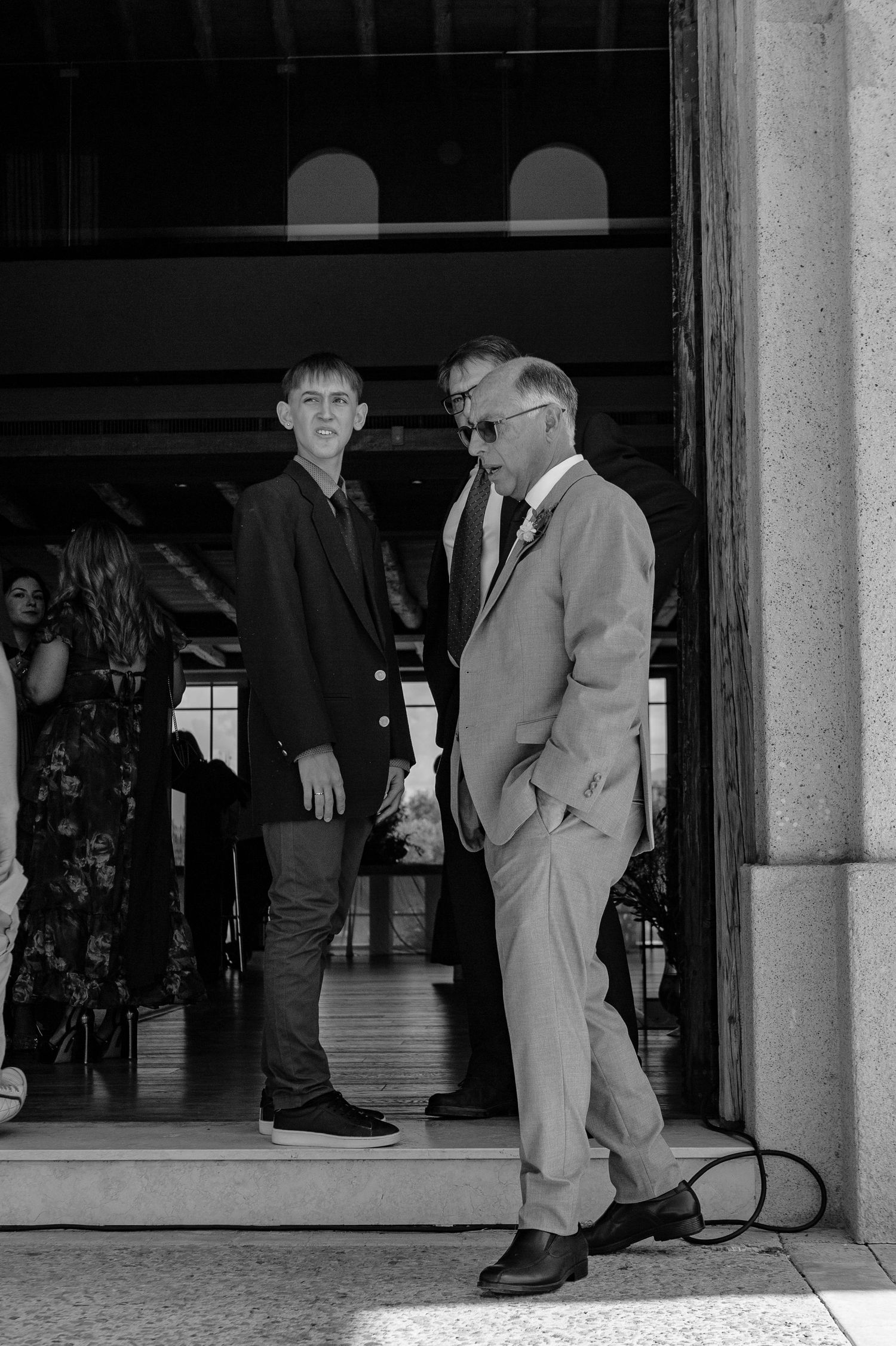 A black and white photo showing two people in formal attire having a conversation in a doorway.
