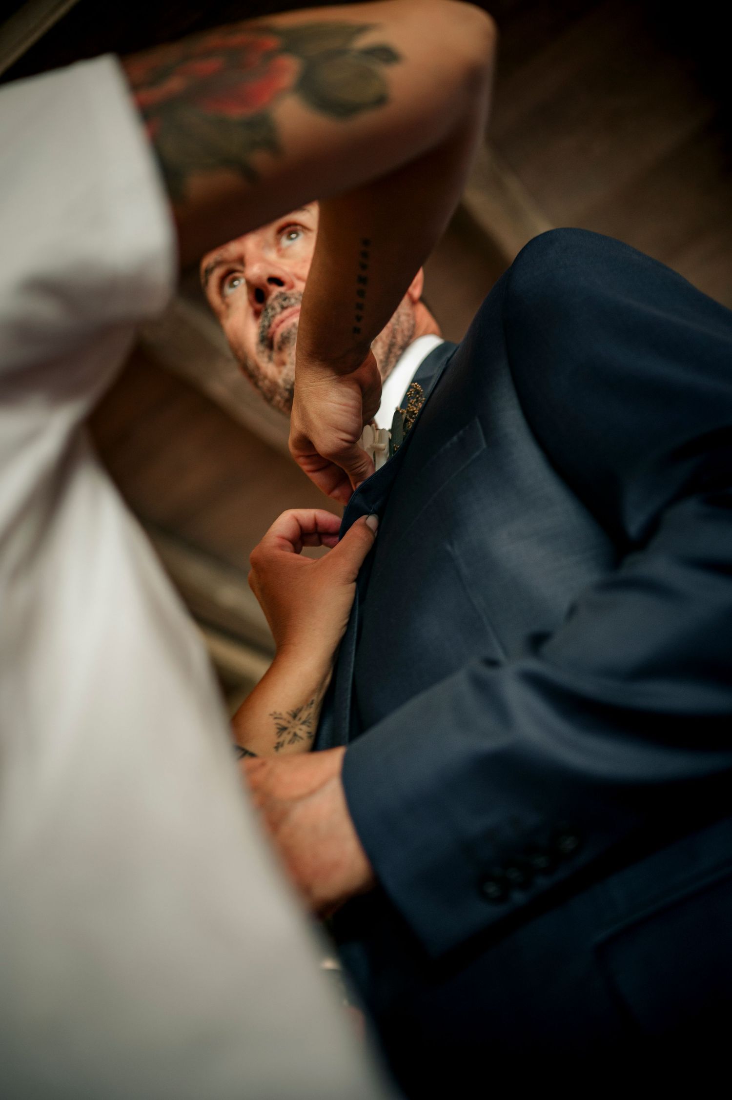 A close-up artistic wedding photograph shows an intimate moment in a navy suit with soft lighting and shallow depth of field.