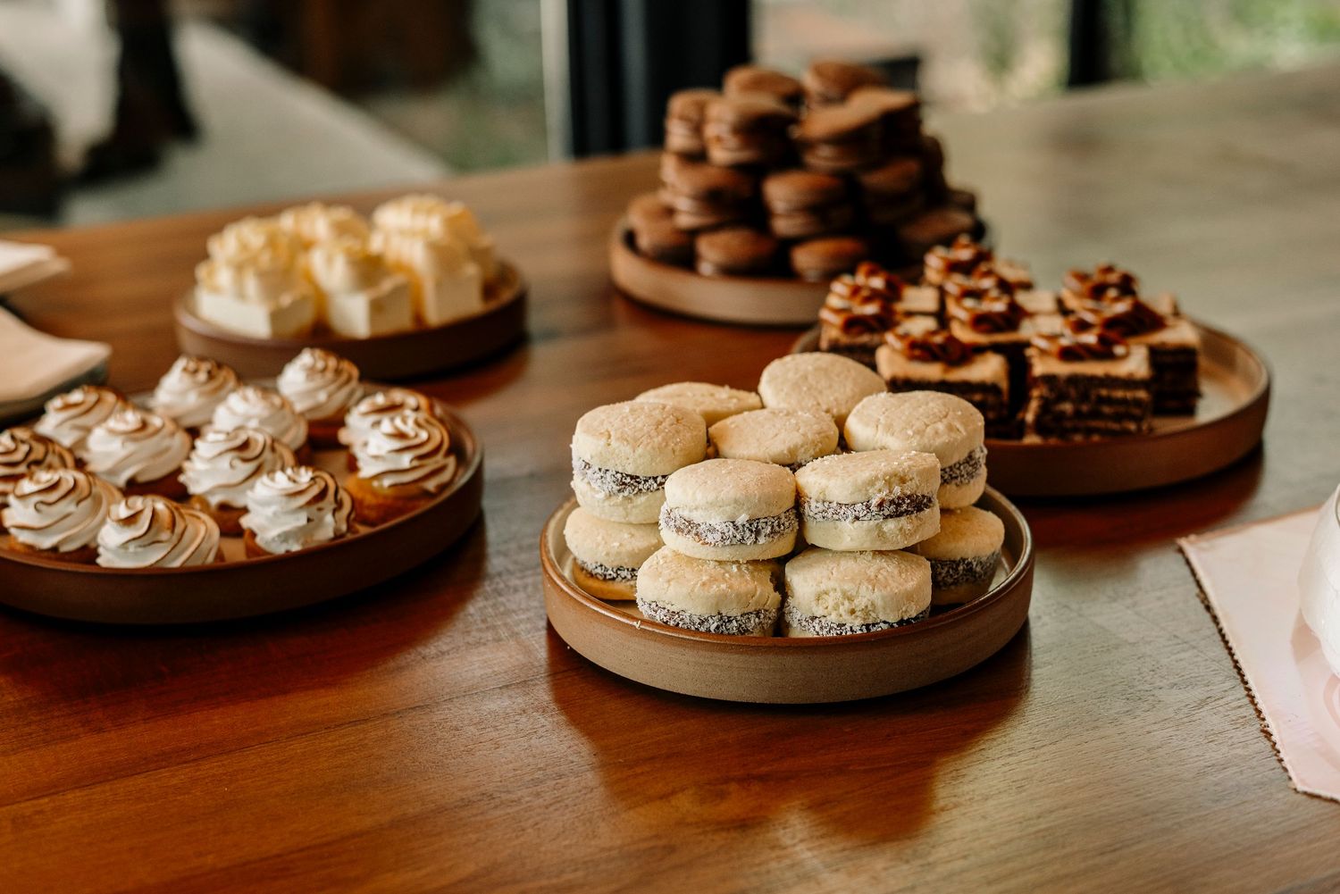 Assorted desserts including macarons, cupcakes, and chocolate treats displayed on wooden serving platters on a table.