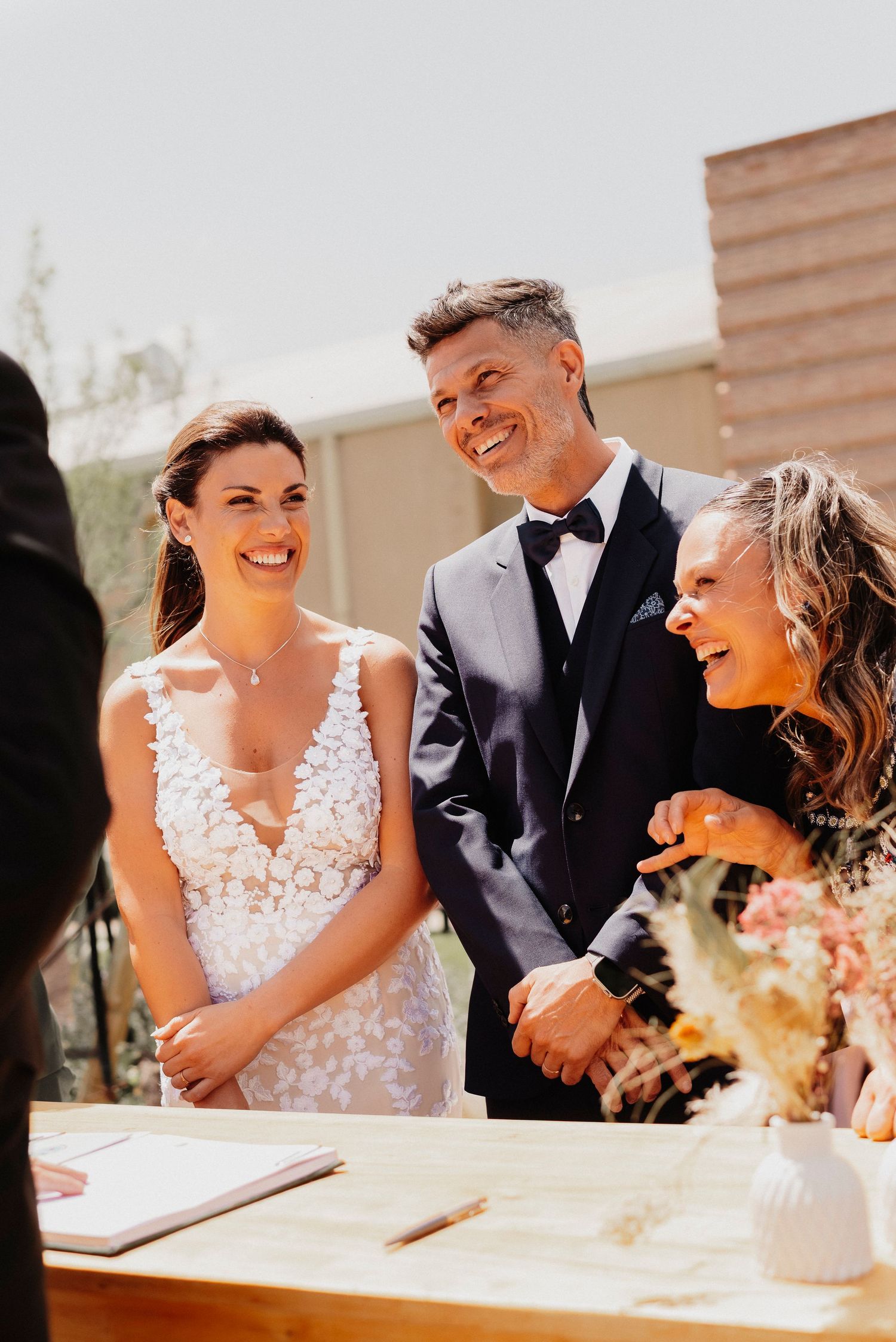 A couple shares joyful laughter while sitting at a table during their outdoor wedding celebration.