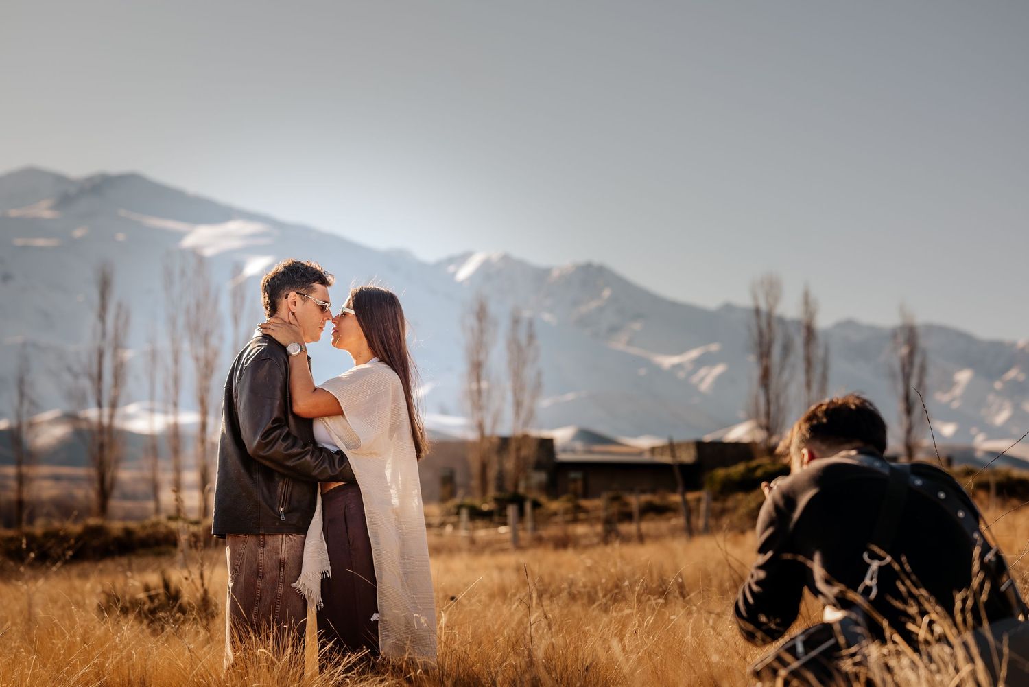 Un fotógrafo capta a una pareja besándose en un campo dorado con montañas nevadas al fondo. preboda en mendoza