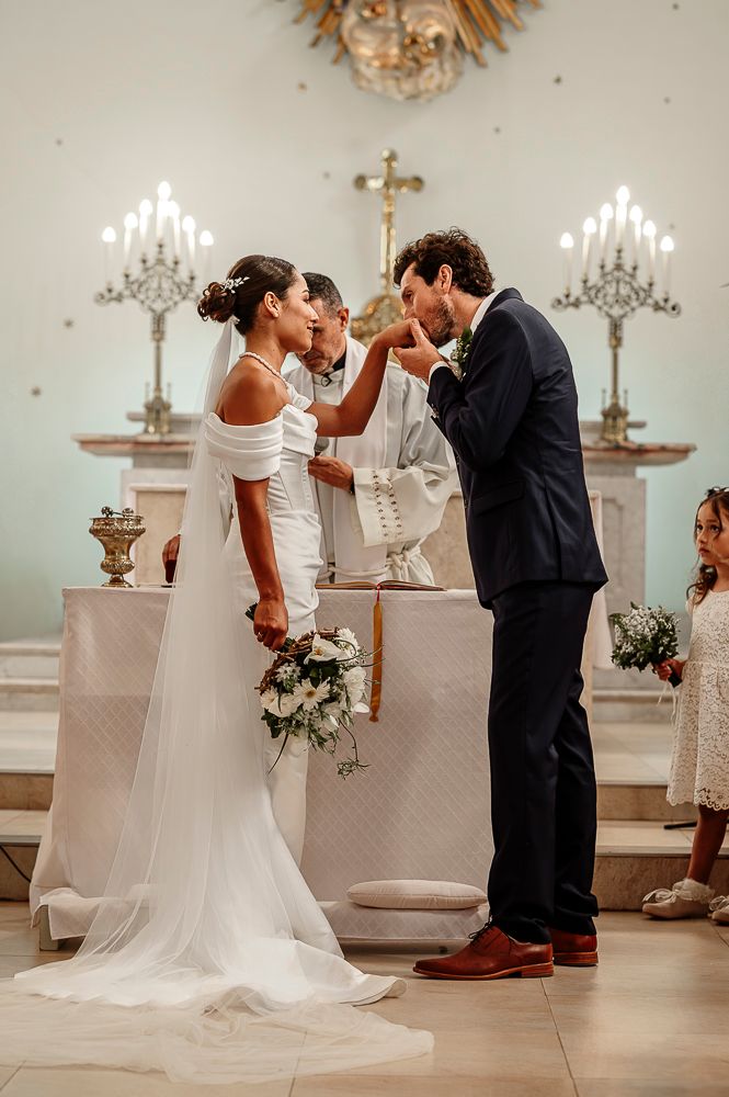 A couple shares their first kiss during a wedding ceremony in an elegant white church with crystal chandeliers. wedding in mendoza