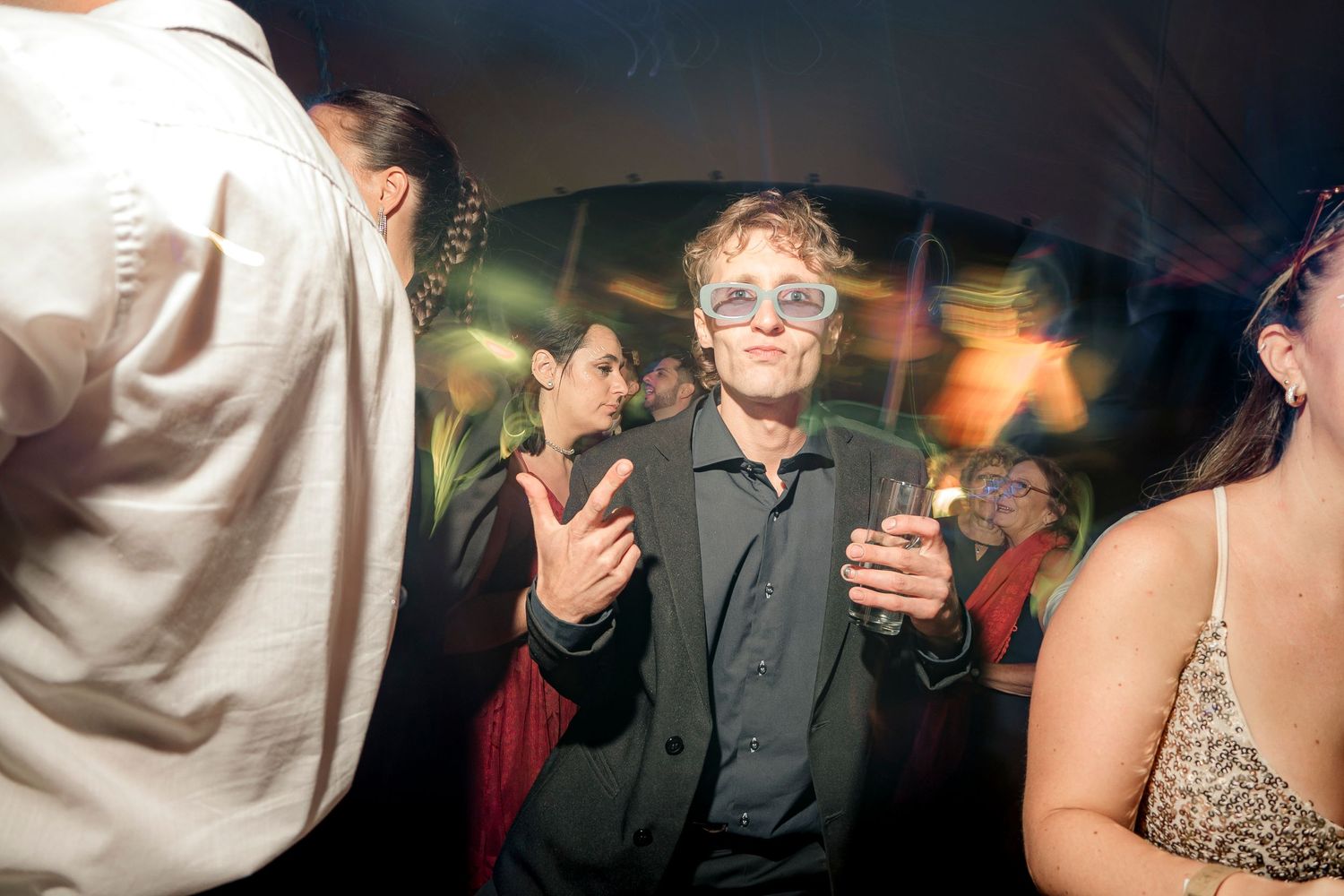 People dancing and socializing at a nightclub or party with colorful lighting and festive atmosphere.