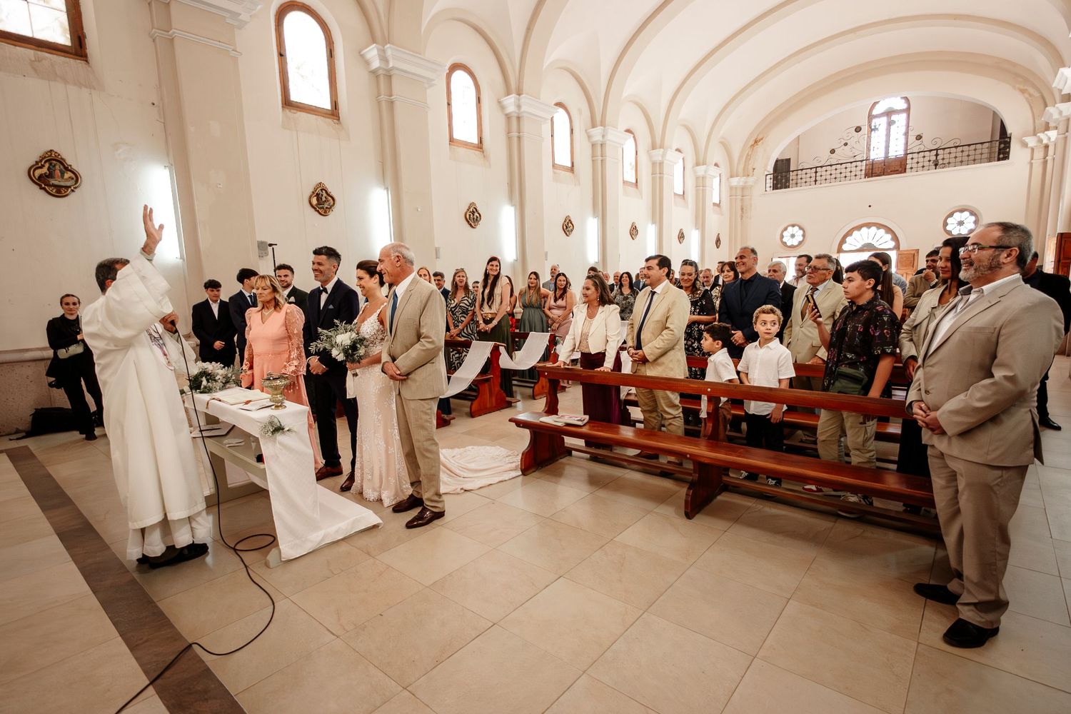A panoramic view of a wedding ceremony inside a grand white church with vaulted ceilings and arched windows.