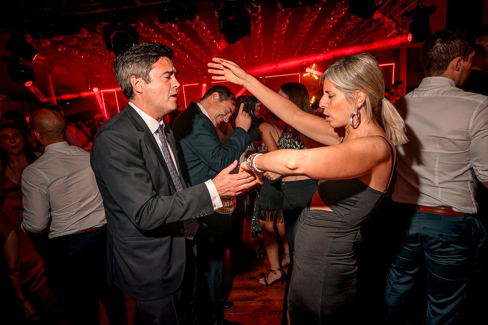 Couples dancing together at a dimly lit party venue with red lighting and formal attire.