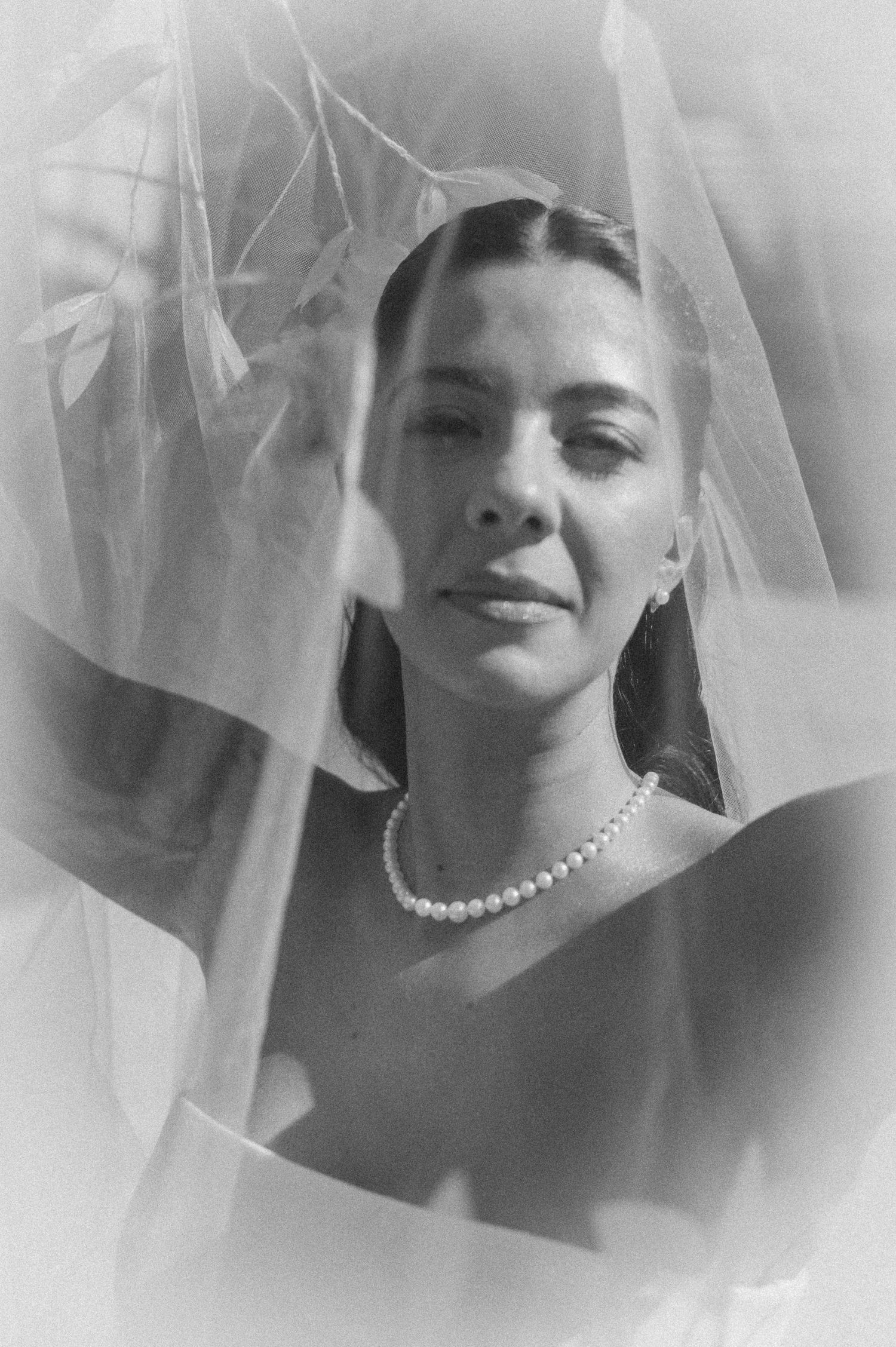 Black and white portrait of a bride wearing a pearl necklace and veil, gazing softly at the camera.