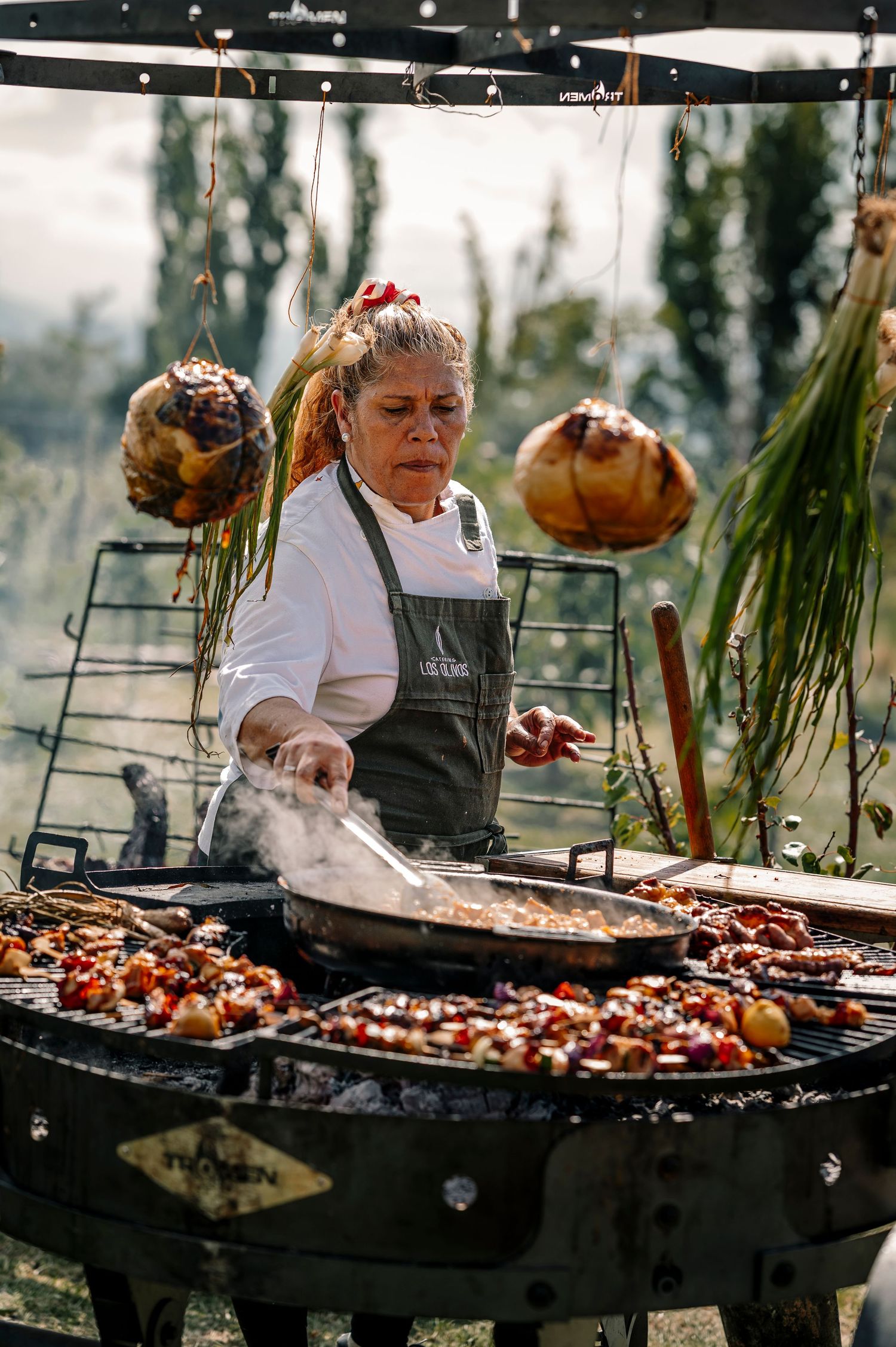 Chef grilling meat on large outdoor barbecue grill with smoke rising during outdoor cooking event.