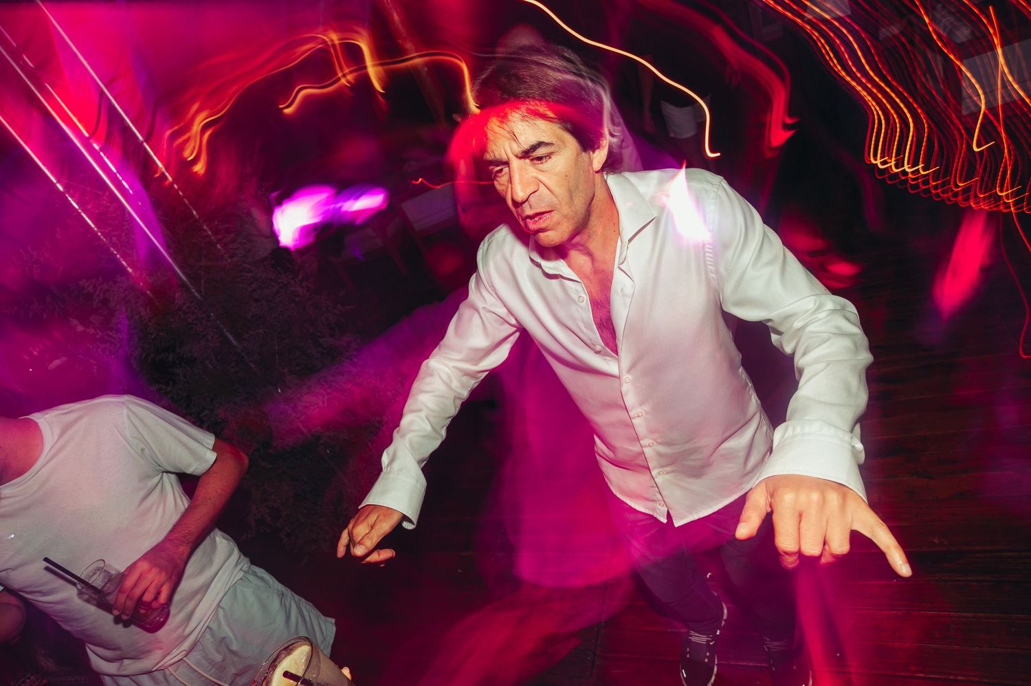 A person in a white button-down shirt dances energetically in a nightclub with pink and purple lighting.