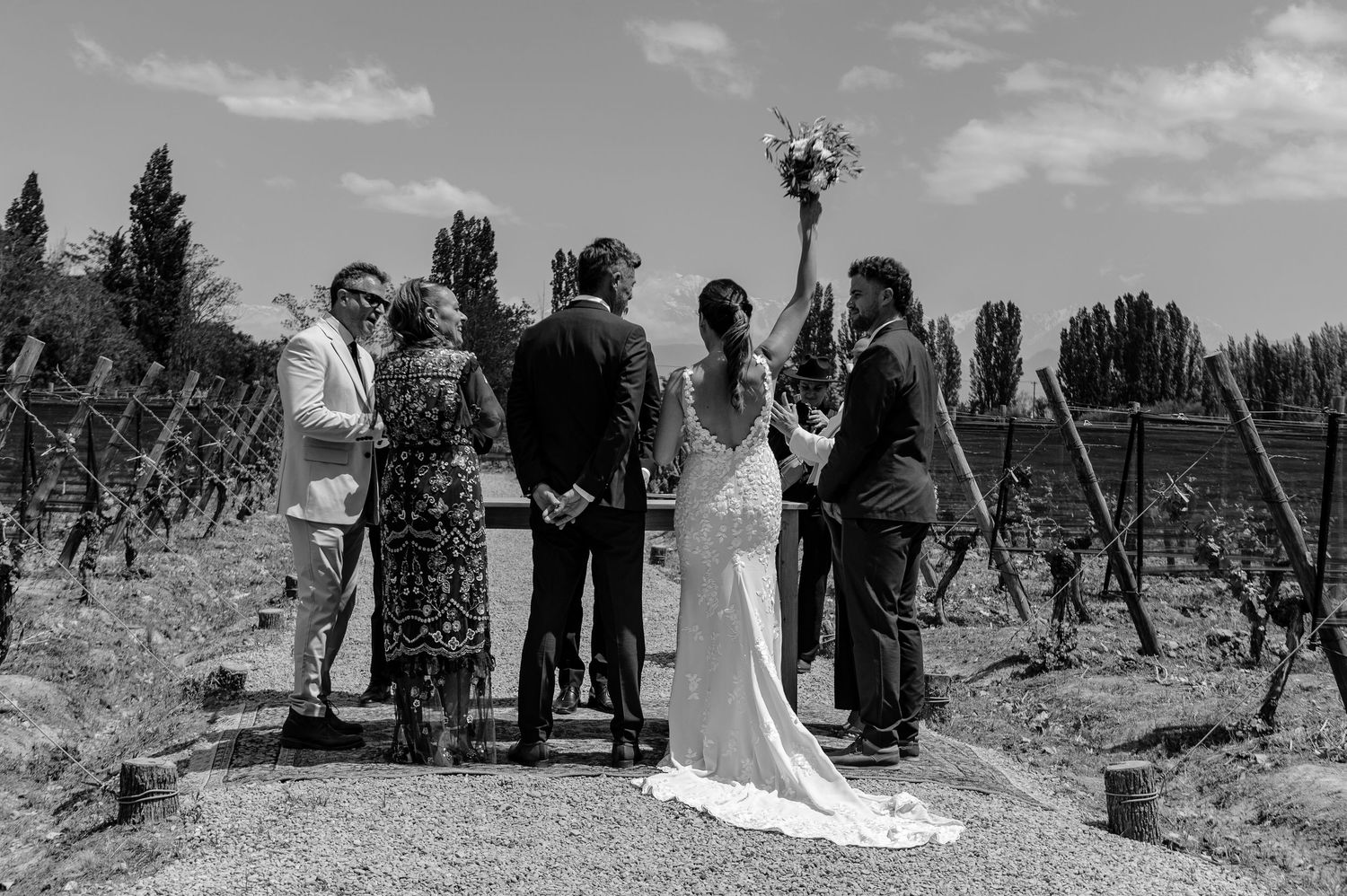 A black and white wedding photo collage showing outdoor ceremony moments and group portraits in a natural setting.