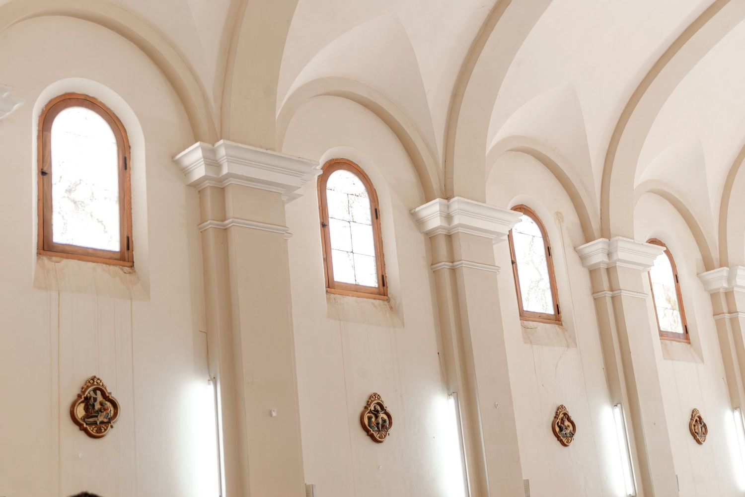 Elegant white arched ceiling with ornate wall sconces and high windows in a historic building interior.