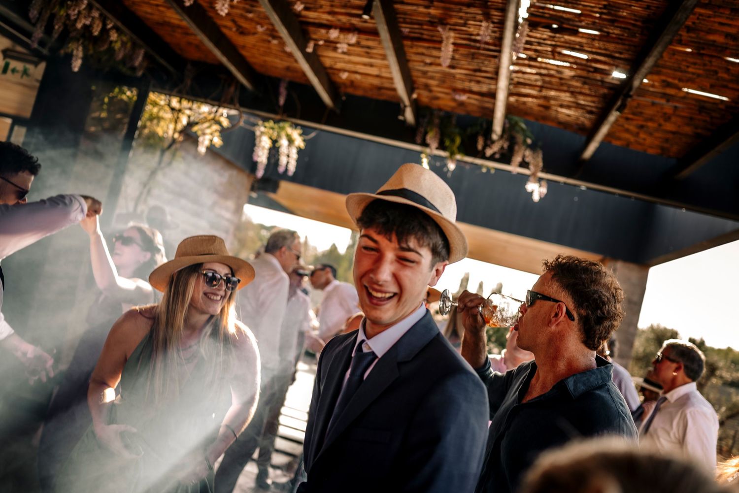 Guests celebrate and dance at a lively indoor party under rustic wooden beams with hanging lights.
