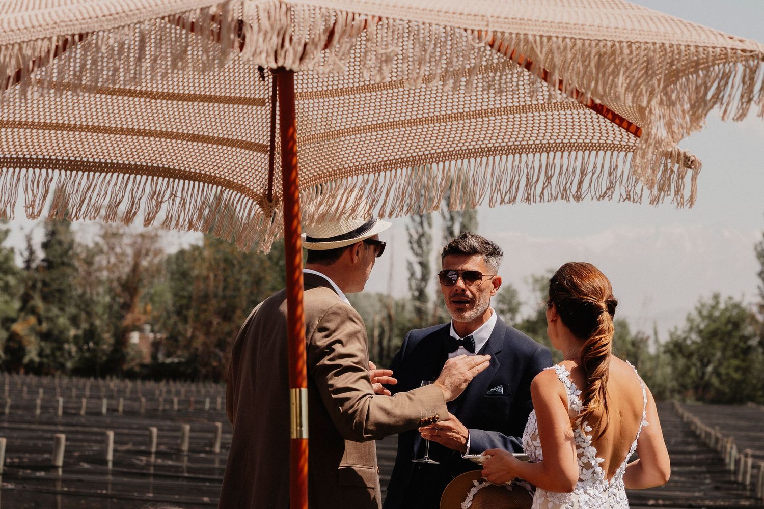 A couple shares a romantic moment under a rustic umbrella during an outdoor celebration.