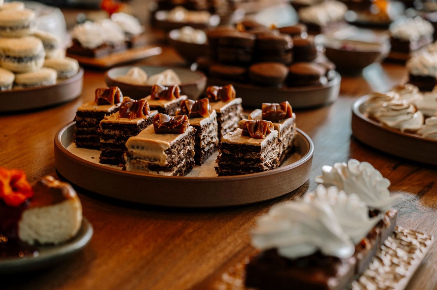 Chocolate dessert bites and pastries displayed on brown plates on a wooden table in warm lighting.