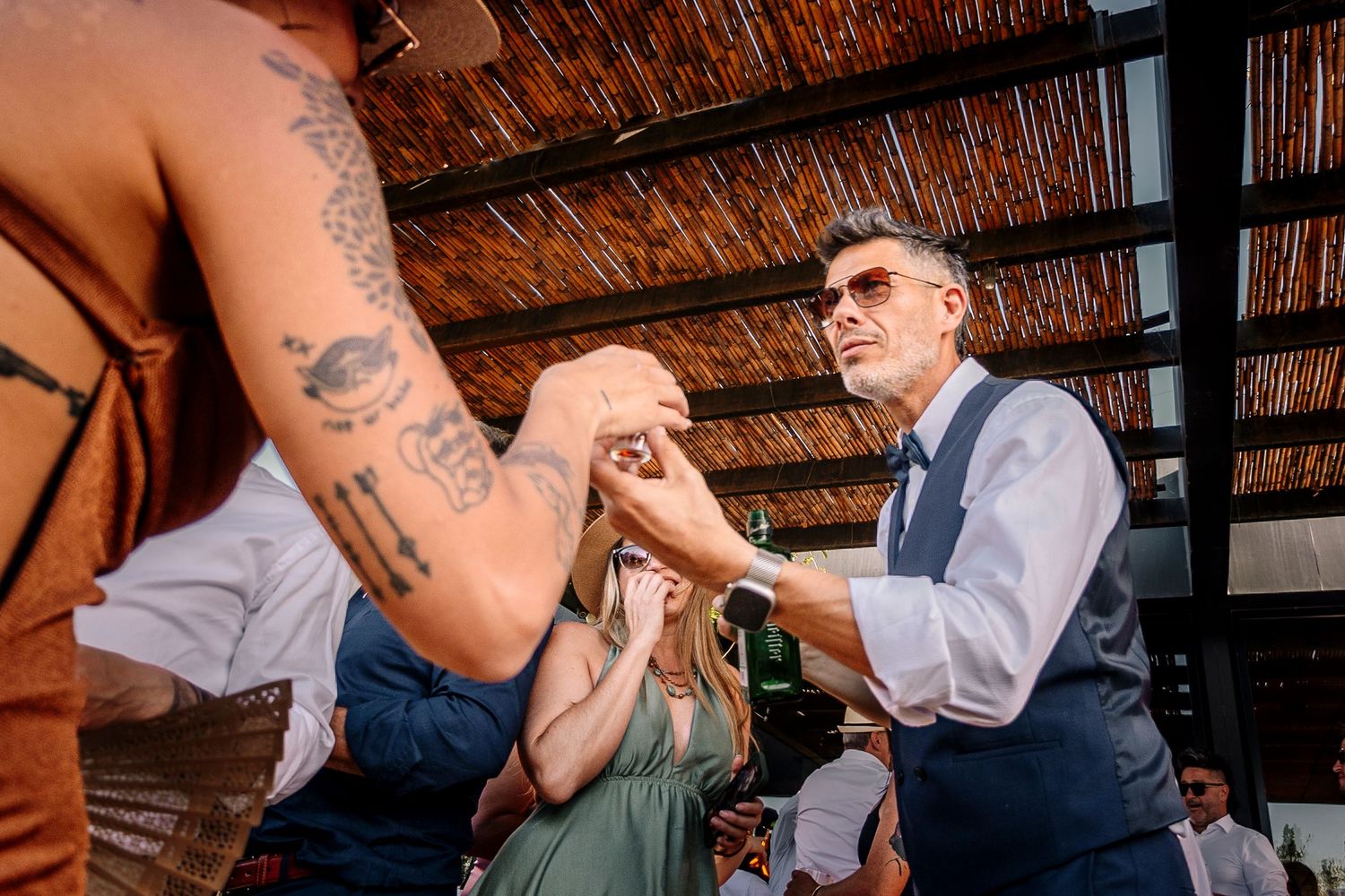 A series of photos showing tattooed arms and hands during an outdoor gathering under a rustic wooden roof structure.