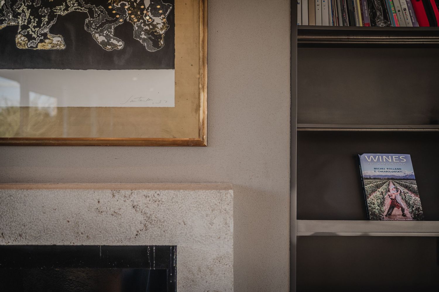 A cozy living room corner with a gold-framed artwork above a stone fireplace and a bookshelf with books nearby.