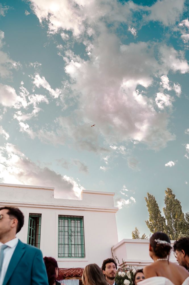 A group gathers outdoors on a sunny day with white clouds and blue sky visible above a white building. wedding in mendoza