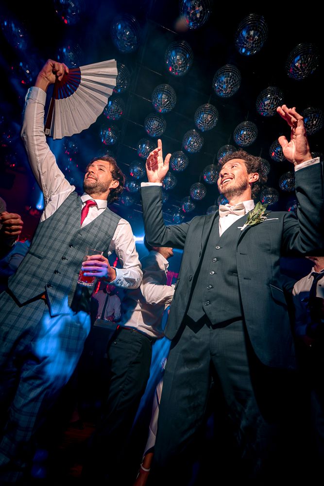 People dancing and celebrating at a nightclub with disco balls and blue lighting in the background.
