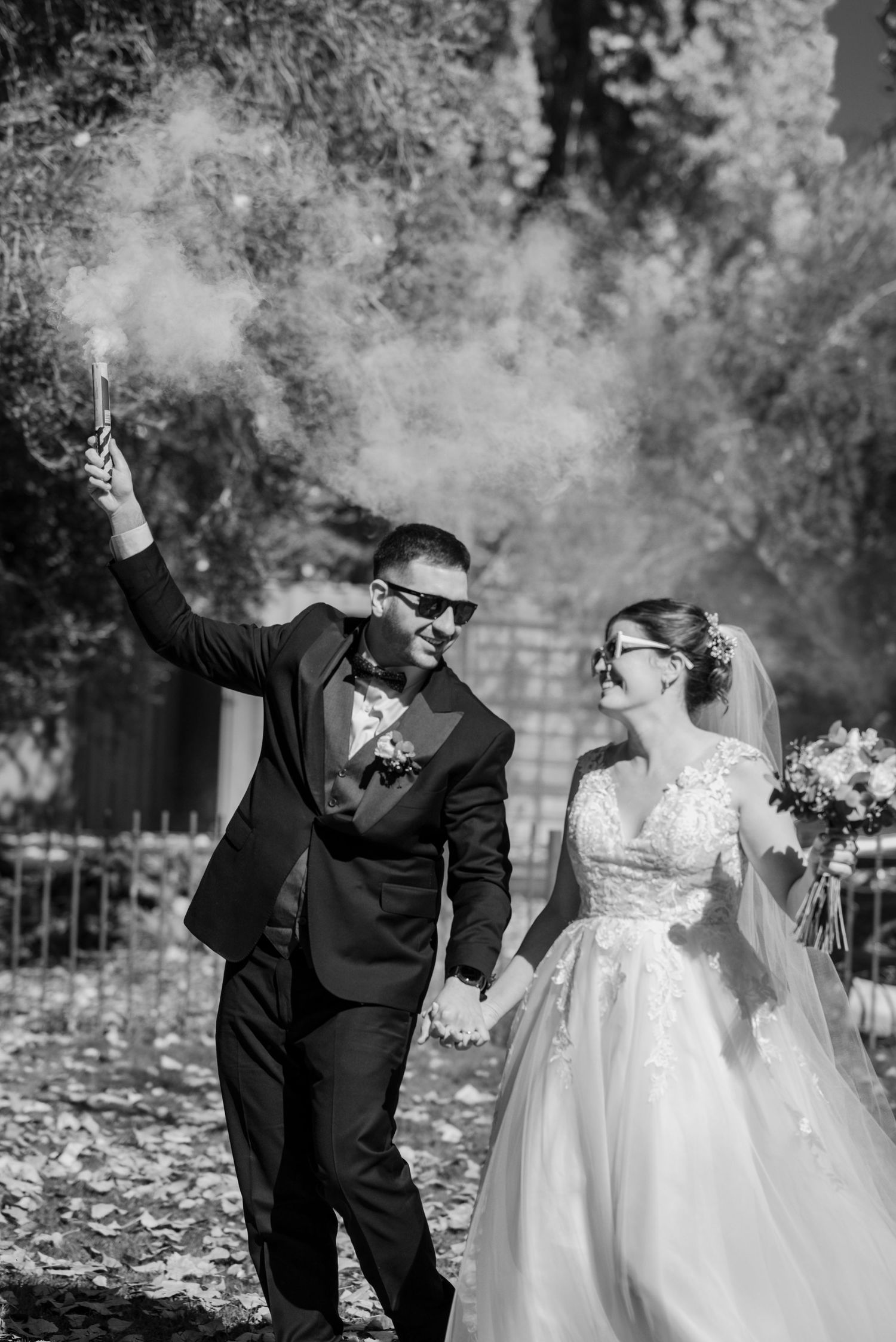 Black and white wedding photo with celebratory smoke effects in an outdoor garden setting.