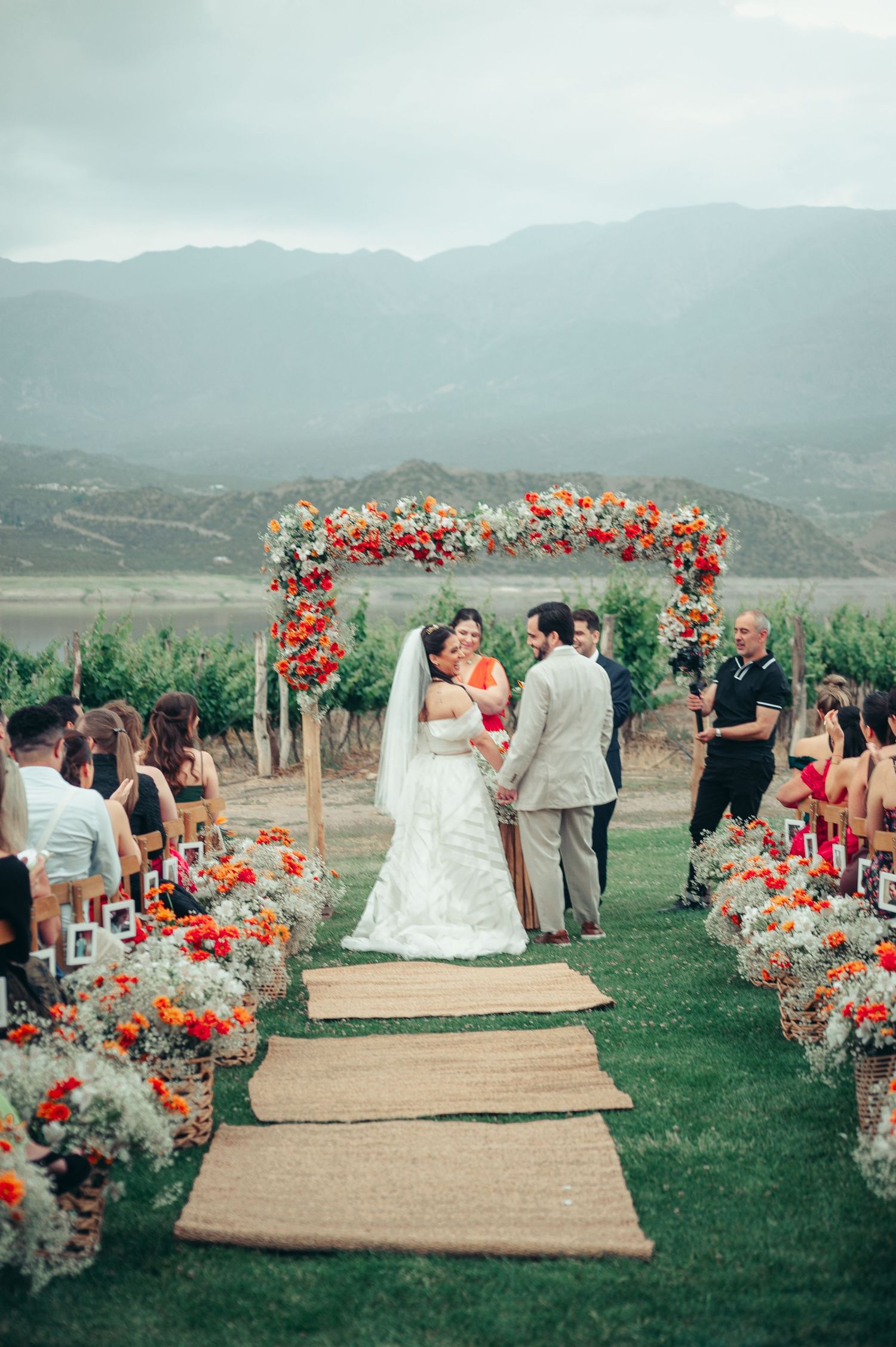 Outdoor wedding ceremony setup with burlap aisle runner and coral floral arrangements against mountain backdrop.