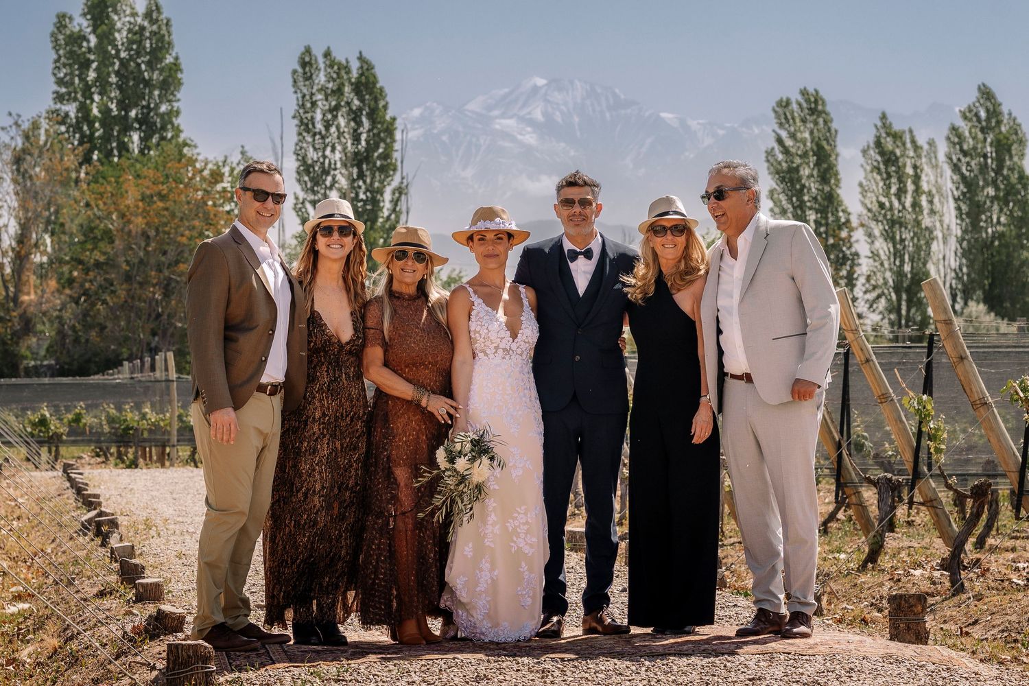Wedding party poses together in a rustic vineyard setting with tall trees and autumn colors in the background.