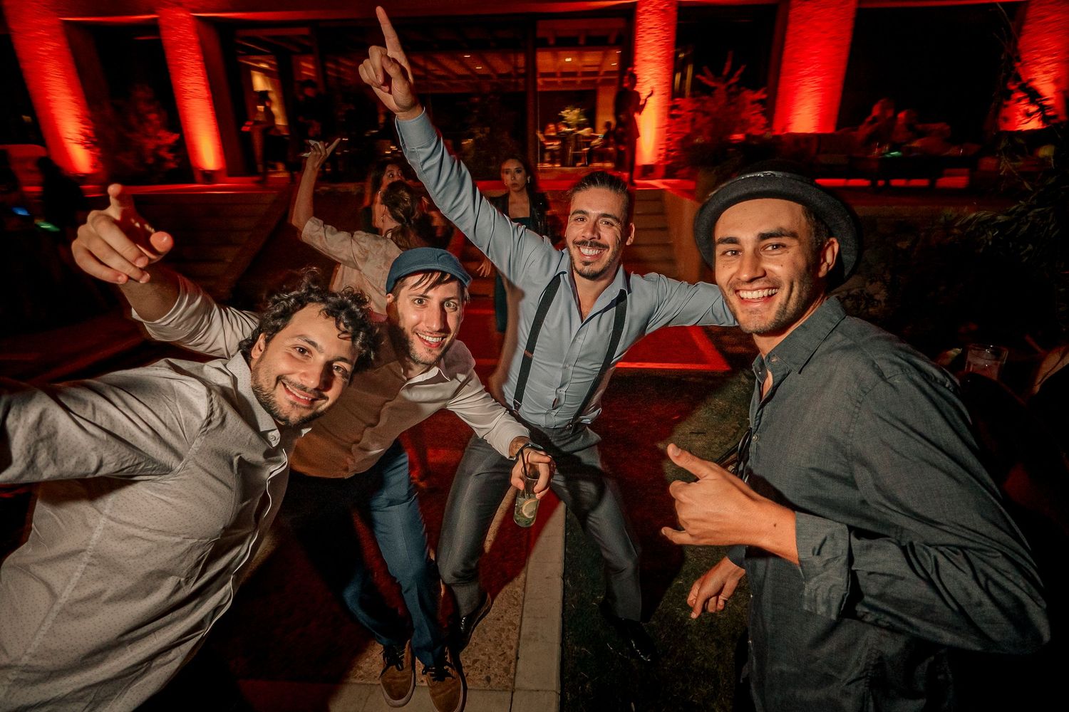 People dancing and celebrating at a lively party with red lighting and energetic atmosphere.