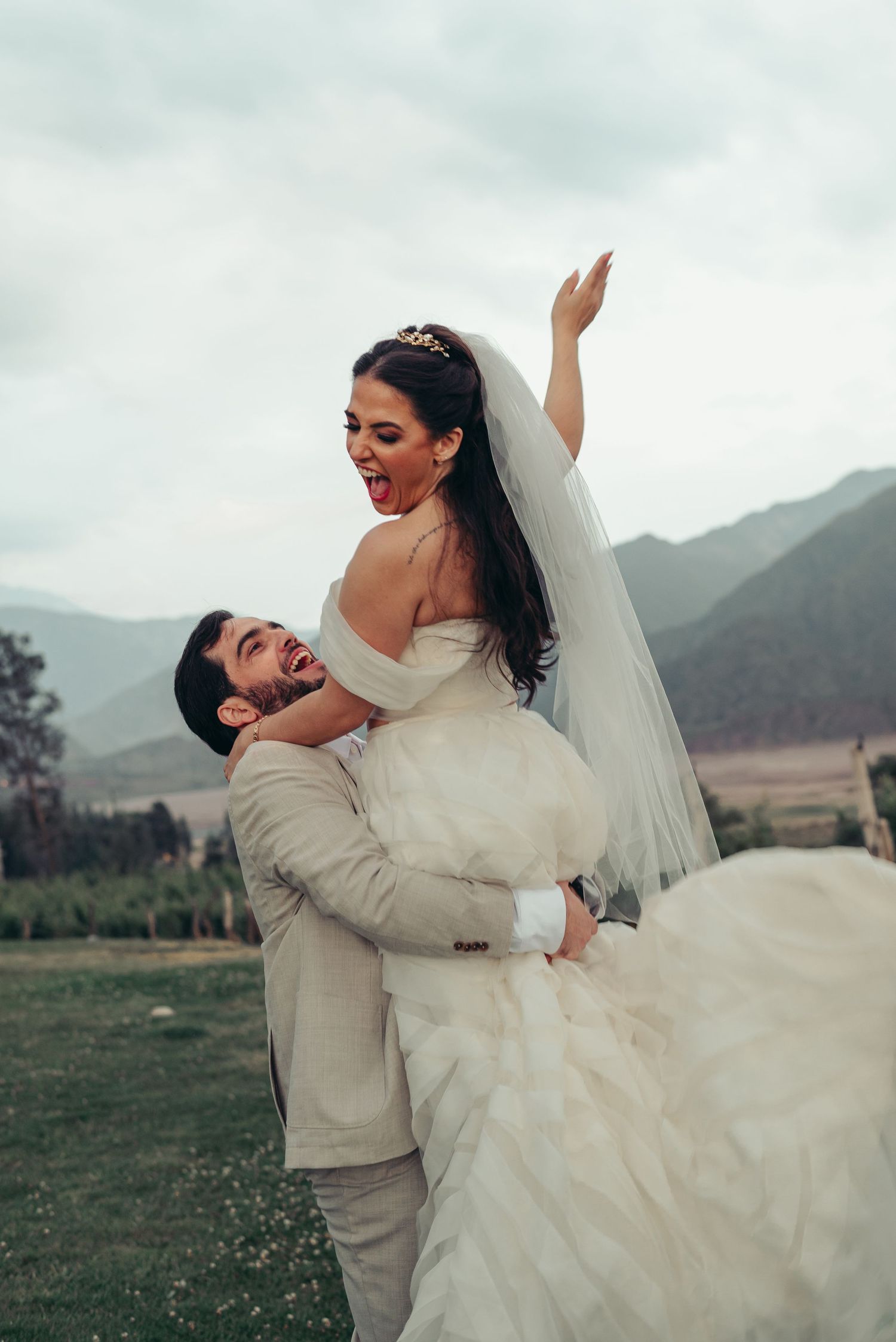 A romantic wedding couple dances and twirls together in a field with mountains in the background.