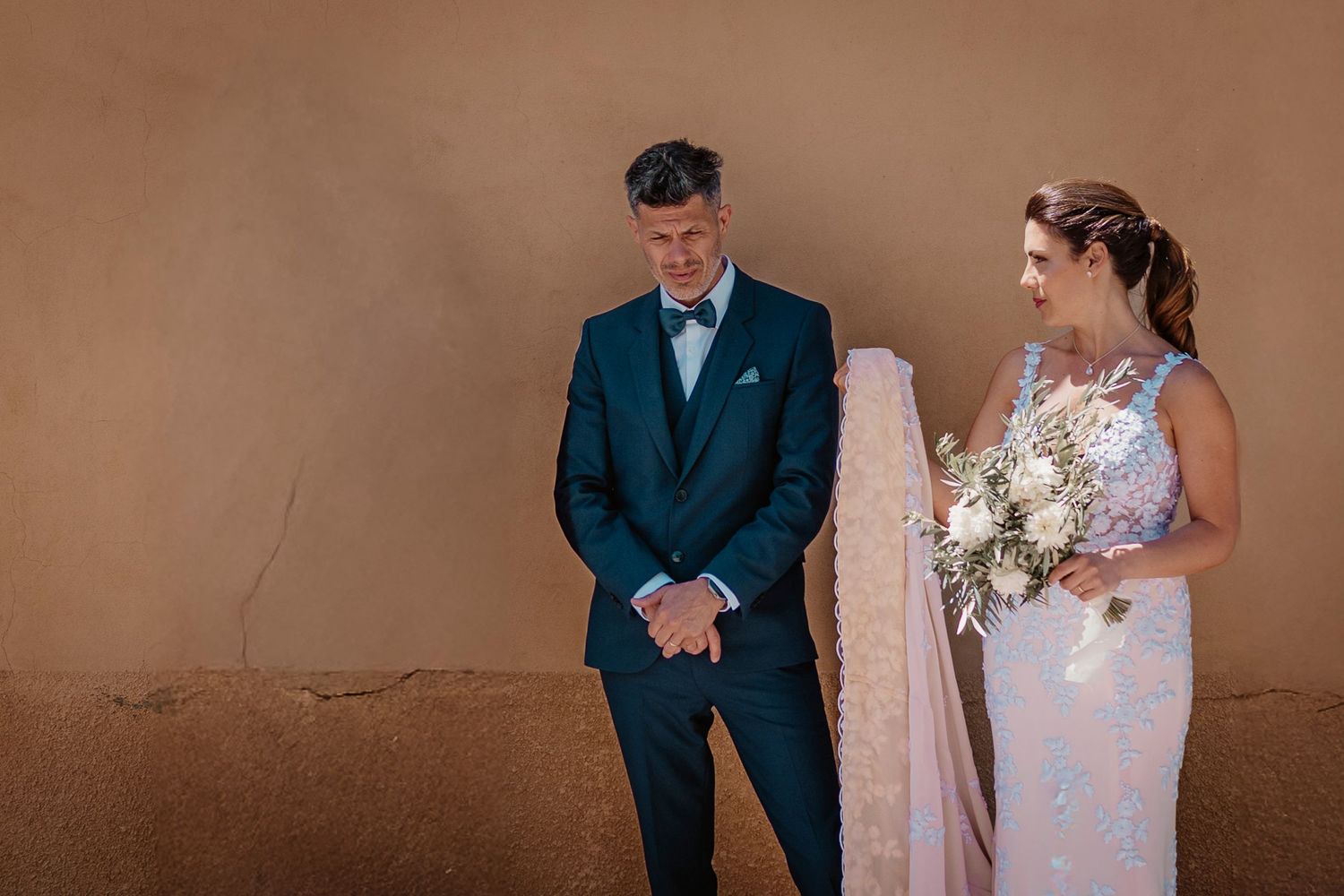 A couple shares a candid moment together during their wedding photo session against a neutral brown backdrop.