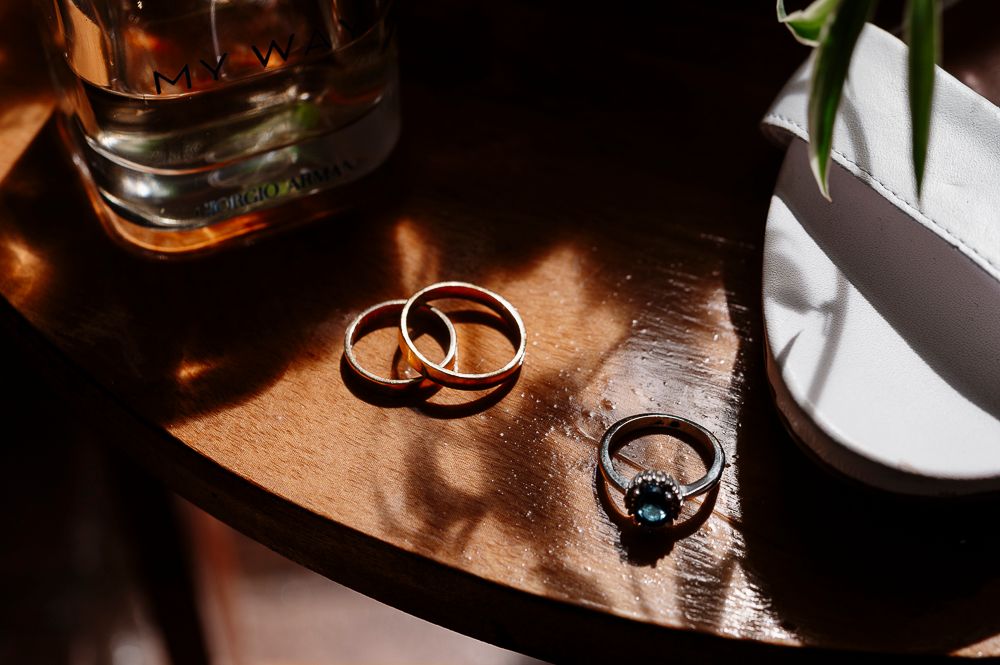 Two gold wedding rings casting dramatic shadows on a wooden surface in warm lighting.