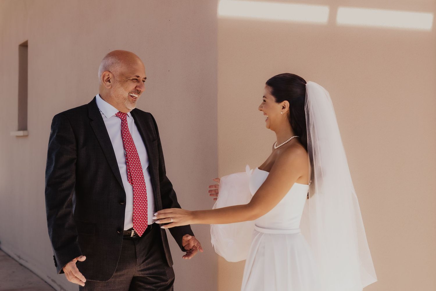 Bride in white gown and veil shares a tender moment with an older man in a black suit and red tie.