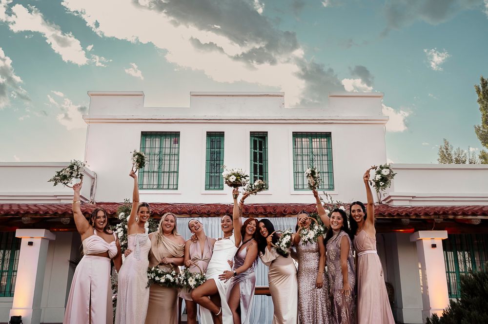 Wedding party in pink dresses celebrates joyfully on the steps of a white building during a summer day. wedding in mendoza