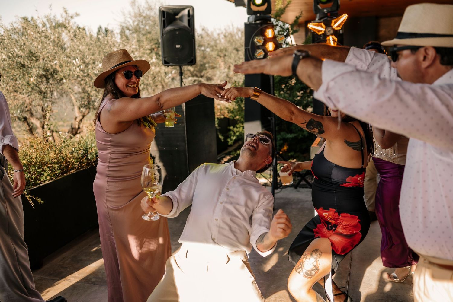 Wedding guests dance together during an outdoor reception celebration with trees in the background.