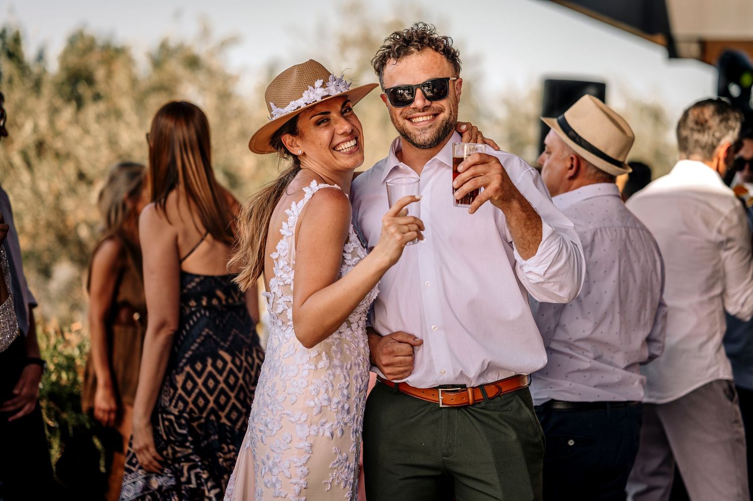 Wedding guests dance and celebrate together during an outdoor reception in natural lighting.