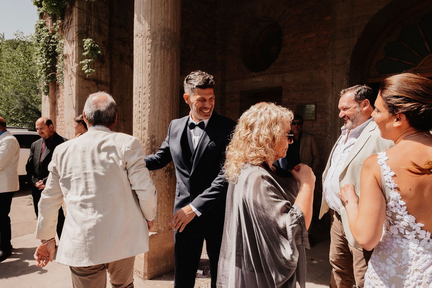 Wedding guests celebrate and dance together in an outdoor venue with stone columns and natural lighting.