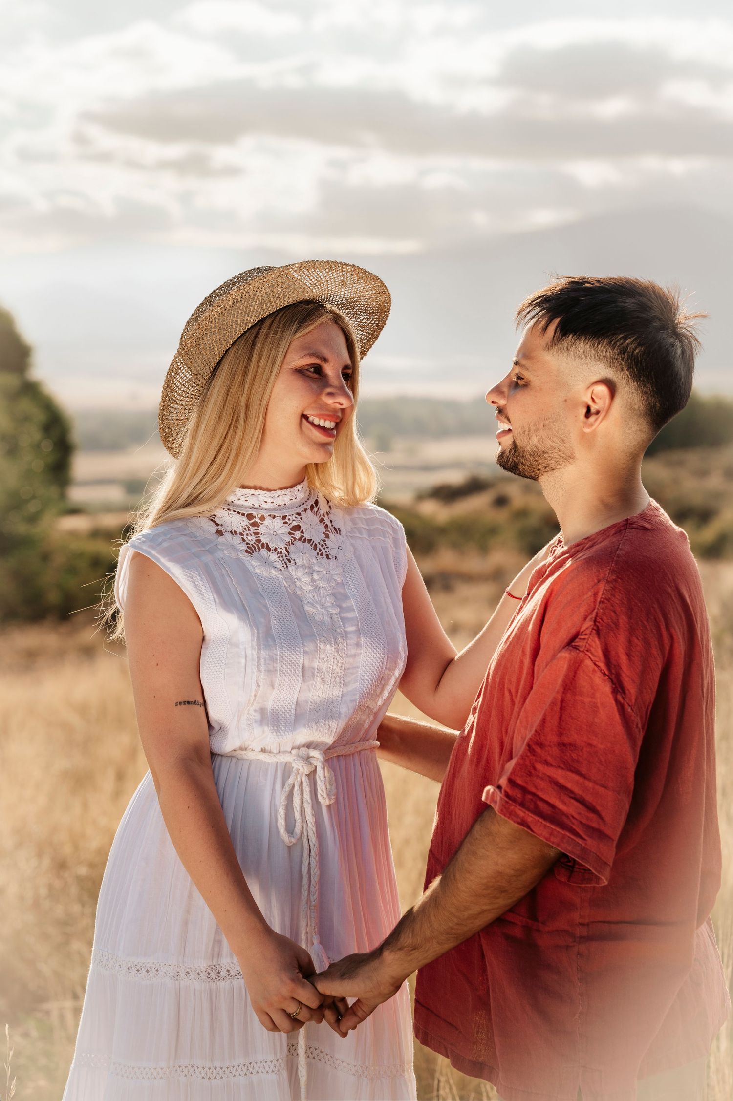 A romantic couple shares tender moments in a sunlit field, with the woman wearing a white dress and man in red shirt.