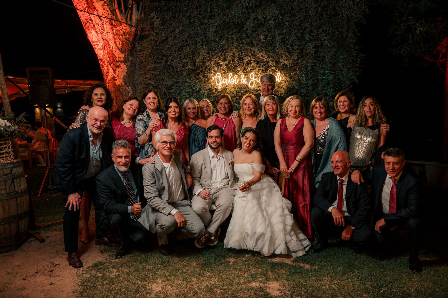 Wedding guests gather together for group photos during an evening reception with warm lighting.