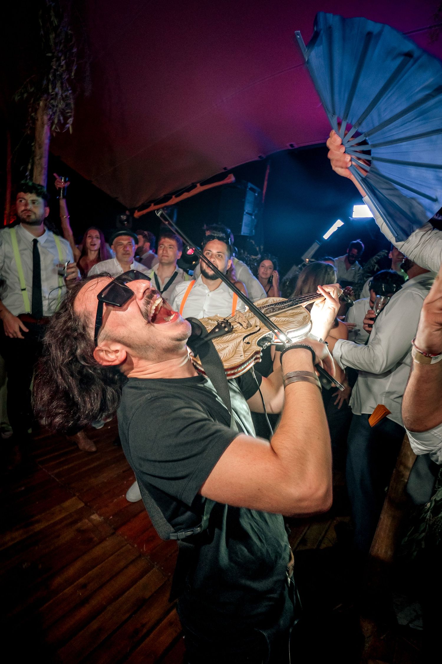 People drinking from blue paper umbrellas at a dimly lit bar party with dramatic lighting and wooden floors.