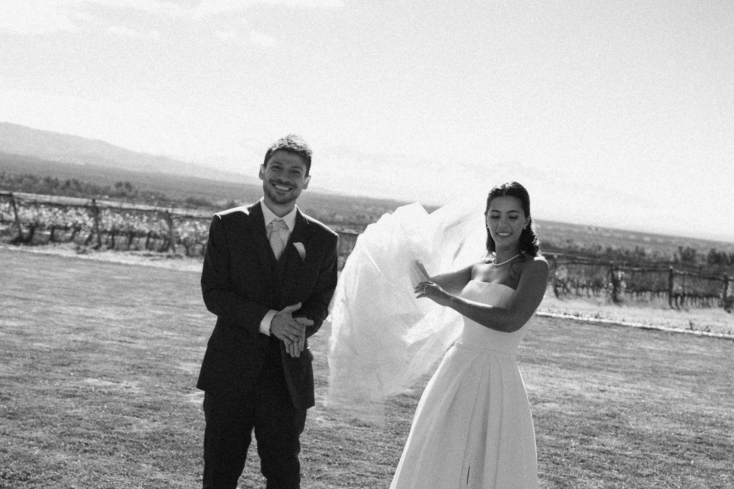 Black and white photo of a bride and groom laughing outdoors at a vineyard wedding venue on a sunny day.