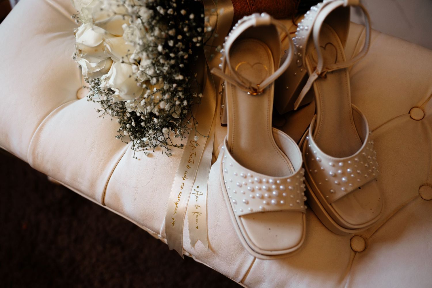 White bridal sandals and wedding accessories with baby's breath flowers arranged on light fabric background.