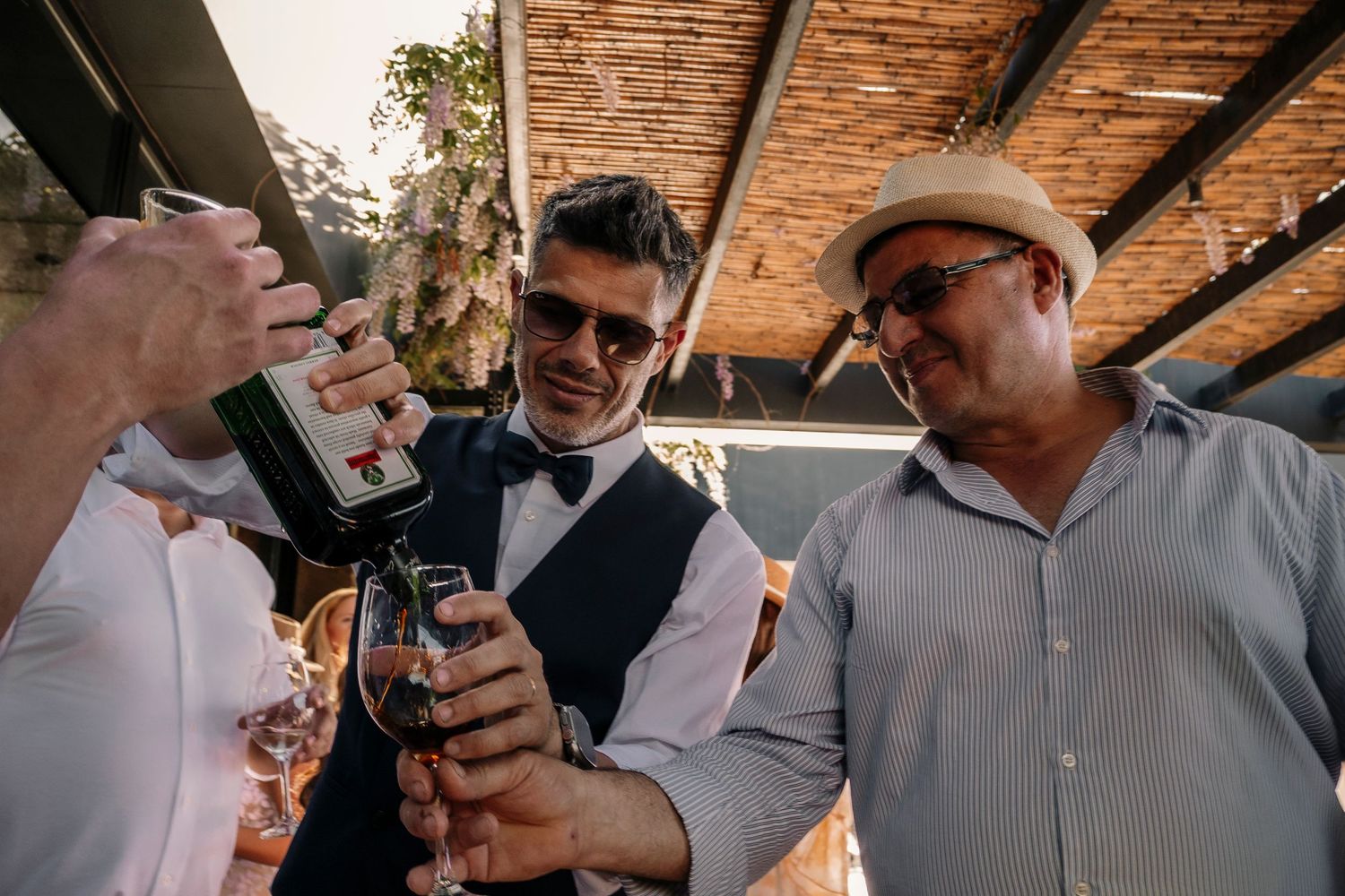 Three people share a celebratory moment pouring drinks at an outdoor venue with wooden beams overhead.