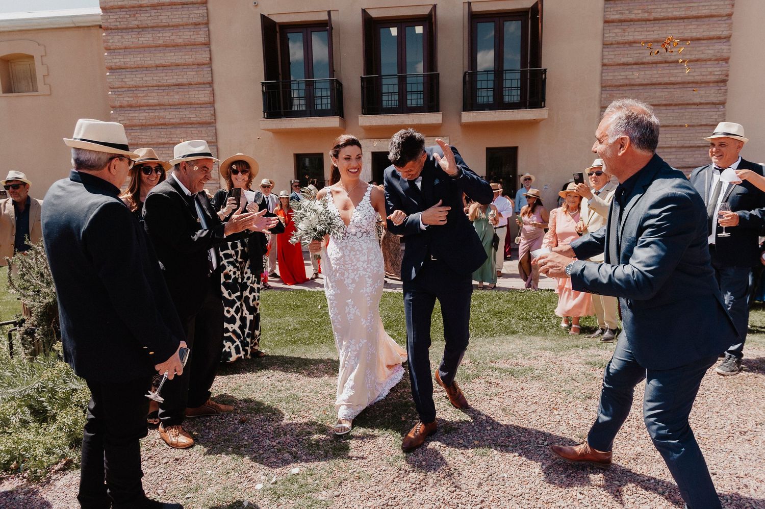 Wedding guests toss flower petals and celebrate during an outdoor ceremony at a rustic venue.