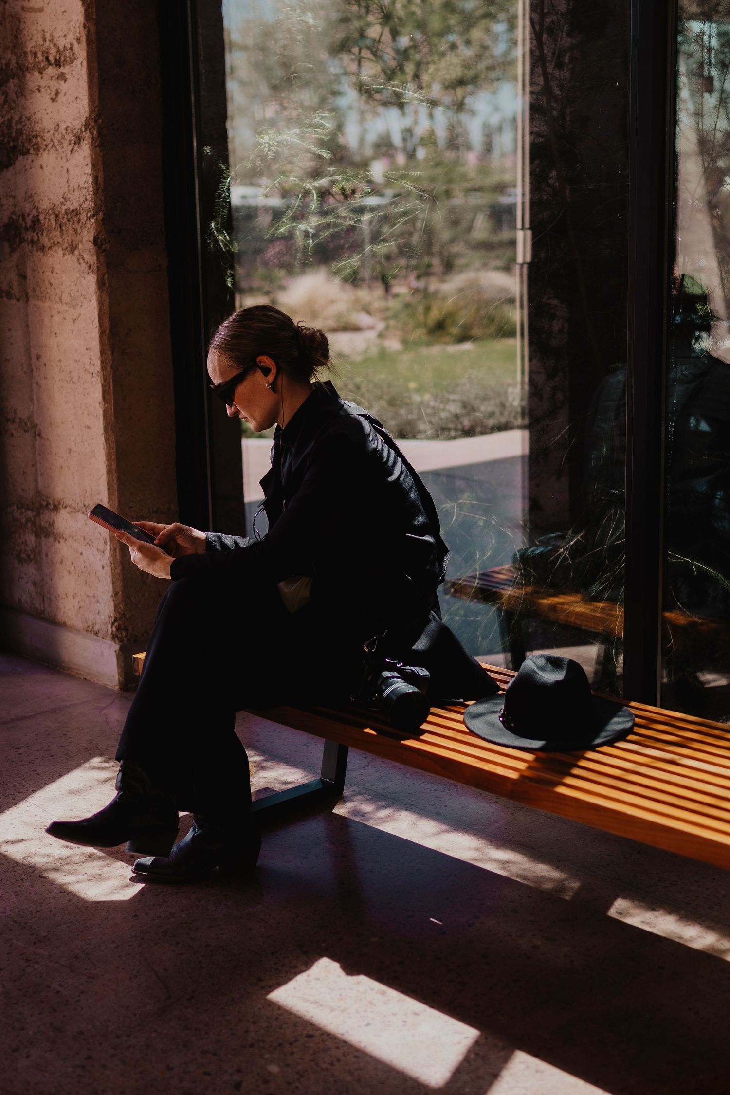 A person sits in a shadowy corner while dramatic sunlight creates striped patterns through window columns.